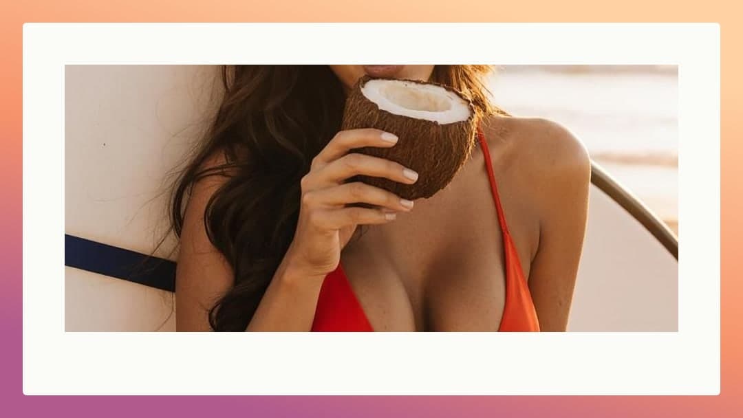 Brunette drinks coconut on beach