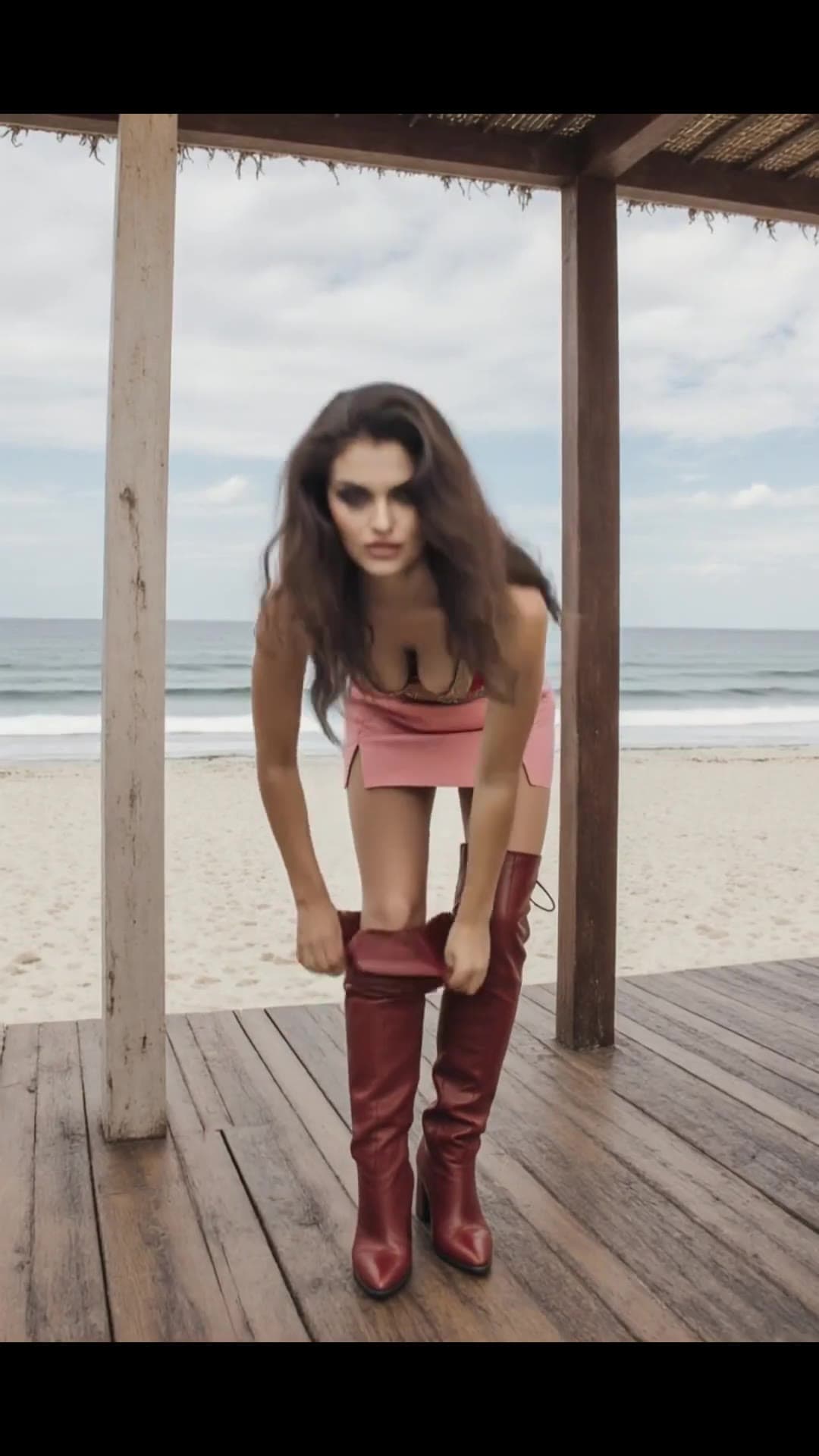 Brunette bends forward pulling boots on beach deck