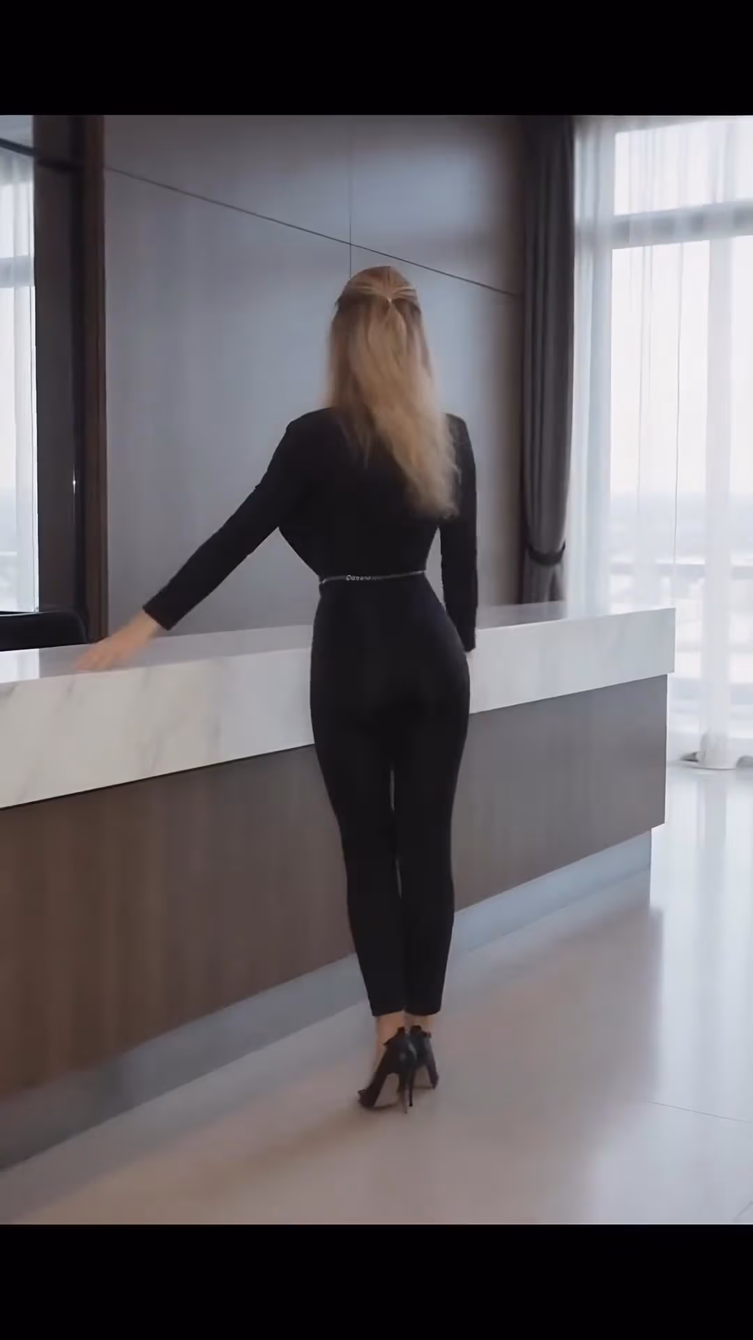 Slim athletic woman leaning over office desk in black jumpsuit